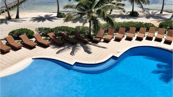 a pool lined with wooden chairs and bordered by the a beach and ocean